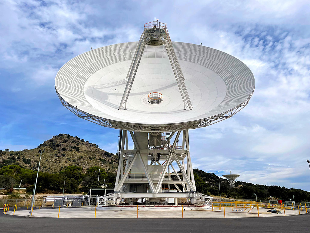 a huge radio telescope dish pointed at a blue sky with white fluffy clouds
